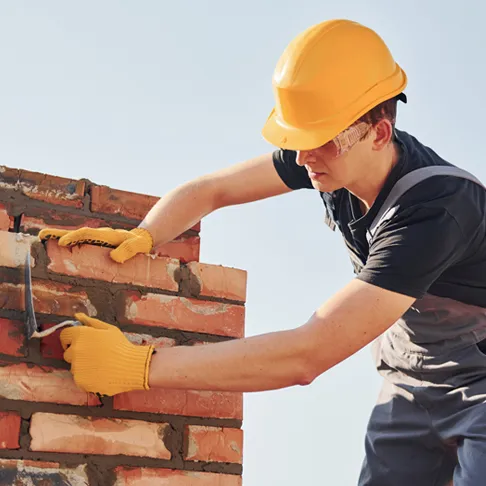 Maurer bei der Arbeit auf der Baustelle beim Verfugen einer Backsteinmauer – professionelles Mauerhandwerk im Hochbau, mit Helm und Arbeitshandschuhen.