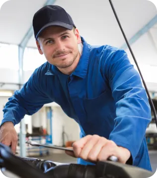Junger KFZ-Mechaniker im blauen Arbeitsoverall mit Cap arbeitet in der Auto-Werkstatt an einem Motor