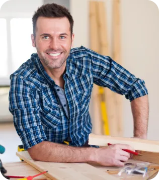Junger Bodenleger im karierten Hemd lächelt bei der Arbeit an einem Holzboden