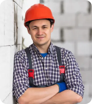Kaminbauer mit rotem Helm und Latzhose vor Ziegelmauer auf der Baustelle