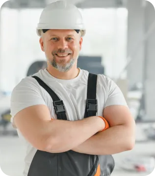 Trockenbauer mit weißem Helm und Latzhose mit verschränkten Armen auf einer Baustelle