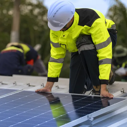 Solarteur in Arbeitskleidung montiert Solarpaneele auf einem Dach. Im Hintergrund arbeitet ein weiterer PV-Experte an der Installation der Photovoltaikanlage