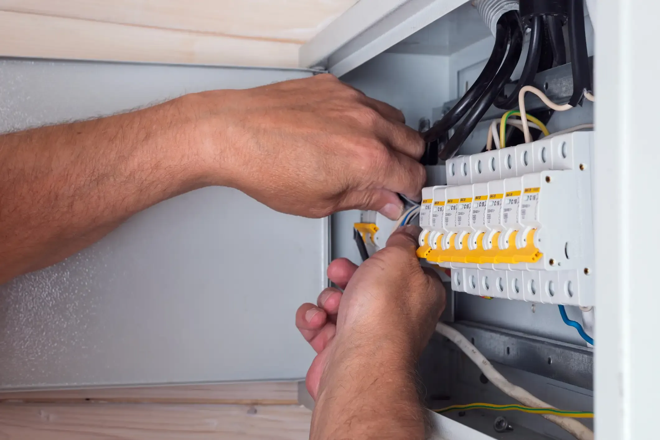 Ein Elektriker führt Arbeiten im Sicherungskasten durch und schließt Kabel an Leitungsschutzschalter im Rahmen einer fachgerechten Elektroinstallation an.