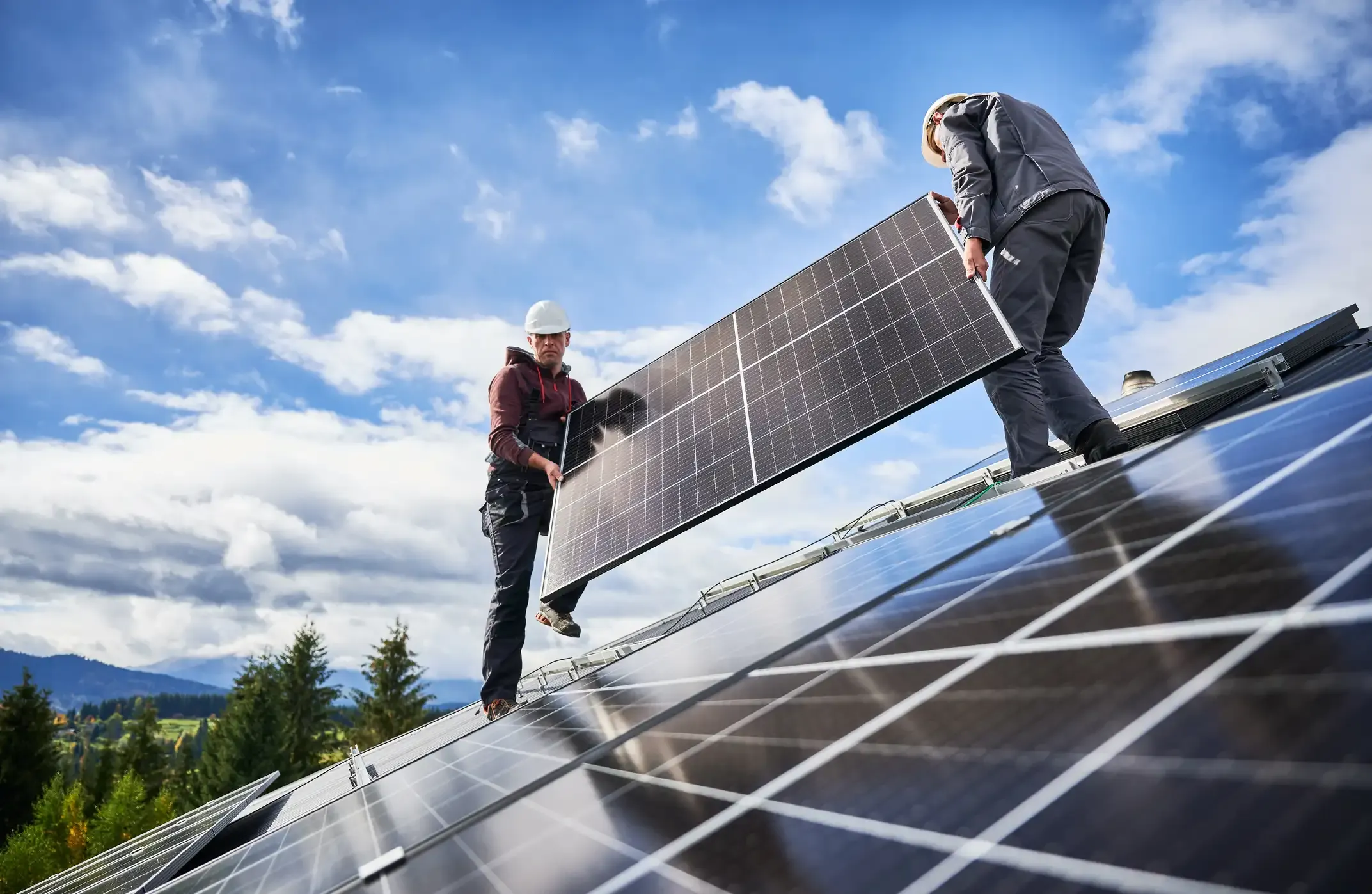 Zwei Solarteure tragen gemeinsam ein großes Solarmodul auf einem Schrägdach, um es im Rahmen einer Photovoltaik-Installation auf dem Montagesystem zu befestigen.