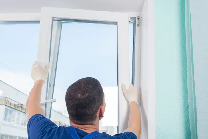 Ein Fensterbauer richtet ein neues Fenster aus und setzt es während des Fenstereinbaus in den Fensterrahmen ein