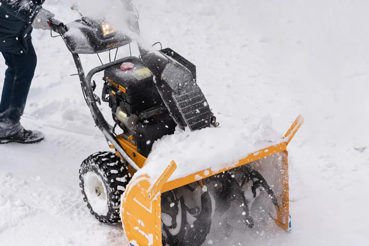 Ein Mitarbeiter eines Winterdienstes räumt mit einer leistungsstarken Schneefräse frischen Schnee von einem Gehweg.