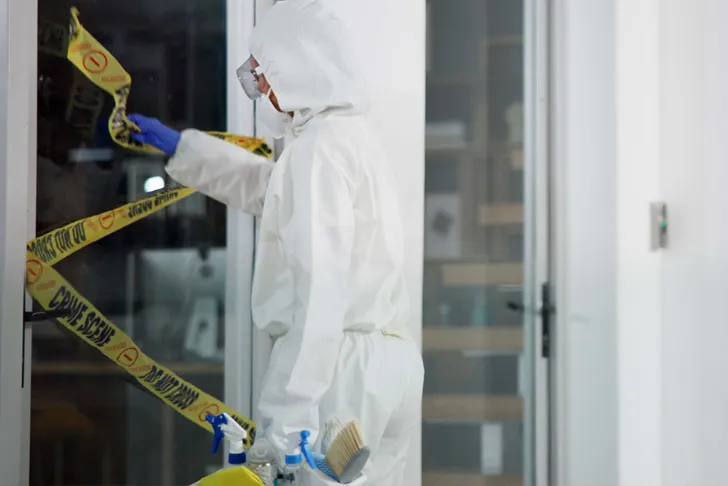 Tatortreiniger in Schutzanzug sichert und reinigt eine Wohnungstür nach einem Todesfall, professionelle Tatortreinigung im Einsatz.
