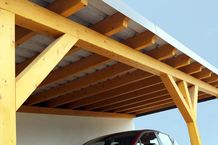 Eine Dachkonstruktion eines Holz-Carports im Bau mit sichtbaren Sparren und Metallverbindungen vor blauem Himmel.