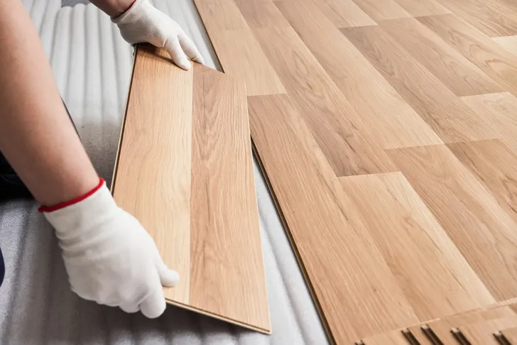 Laminatverleger verlegt Laminatdielen im Klicksystem auf einer Trittschalldämmung und passt eine Diele mit Handschuhen ein.